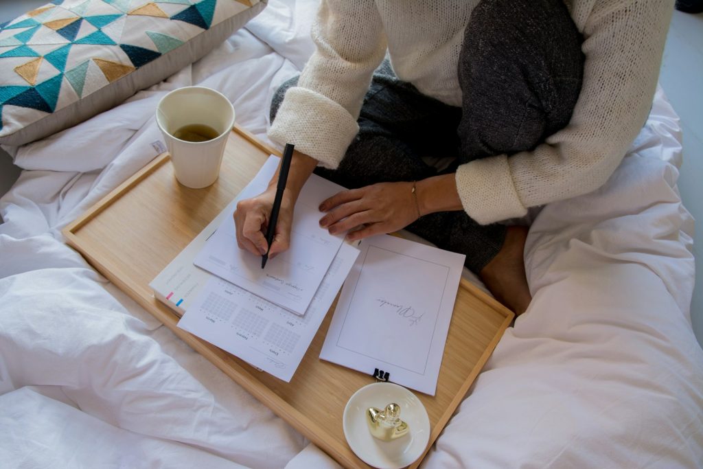 A person writing in a notebook beside a mug on a wooden table